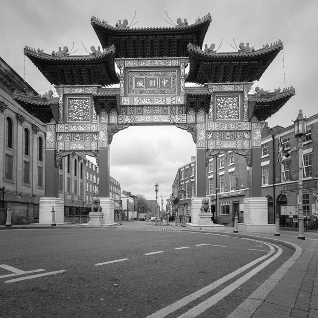 A narrow street in Chinatown decorated with numerous red Chinese lanterns hanging overhead, interspersed with illuminated vertical and horizontal signs featuring Chinese characters in red, yellow, and