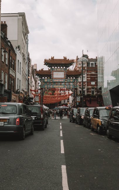 A busy urban street scene in Chinatown near WC2H, showing several multi-storey commercial and office buildings with modern glass facades and traditional brick facades. On the ground level, there are s